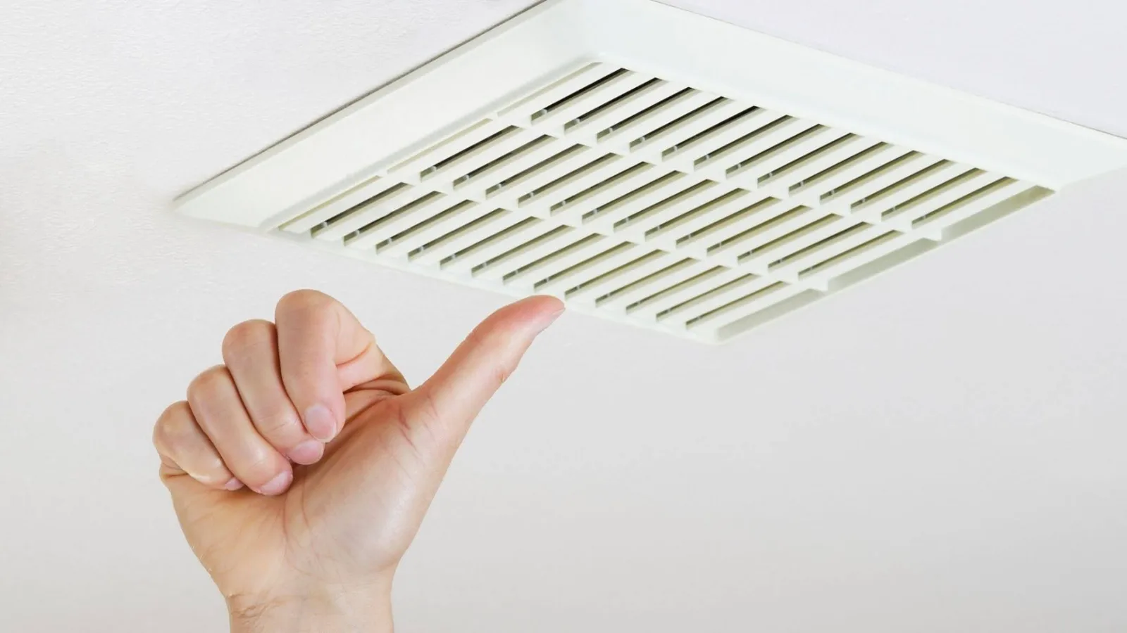 Hand pointing toward a whole house fan ceiling grille that draws indoor air upward