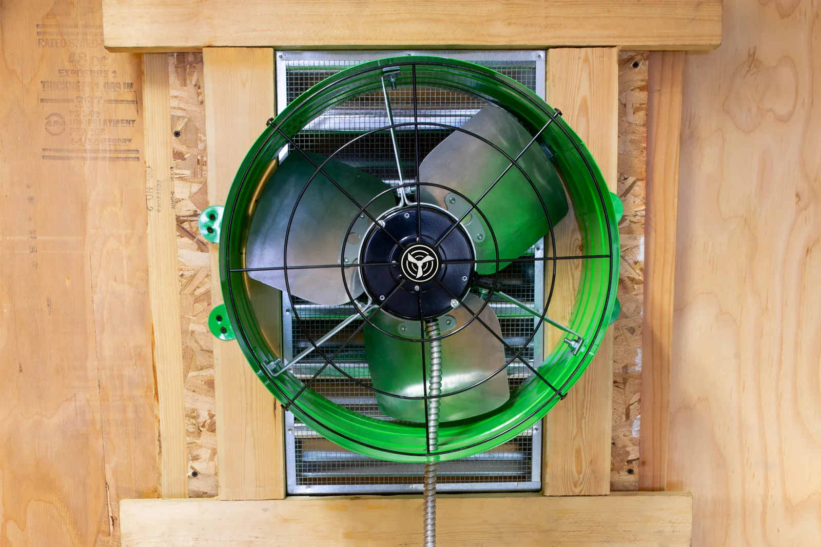Green QuietCool attic fan mounted in wooden attic framing
